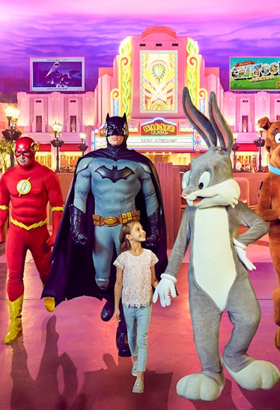Child walking with Warner Bros characters at Abu Dhabi theme park.
