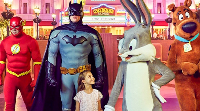 Child walking with Warner Bros characters at Abu Dhabi theme park.