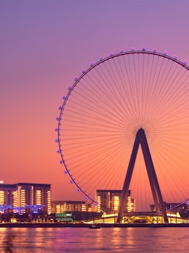 Ferris wheel at sunset in Dubai with city lights in the background.