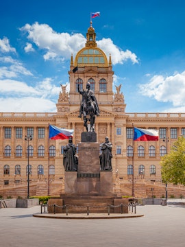 Equestrian statue in front of Prague National Museum with Czech flags.