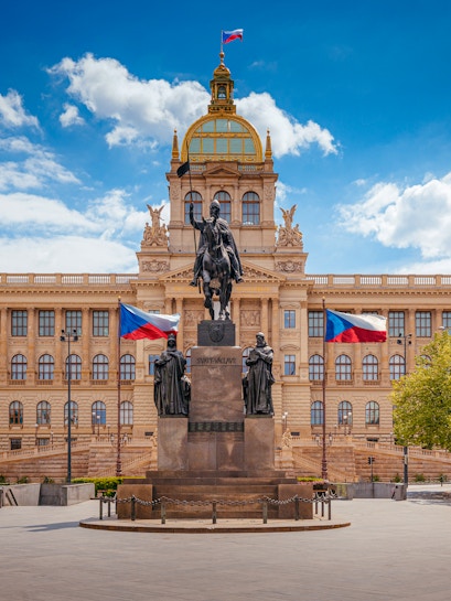 Equestrian statue in front of Prague National Museum with Czech flags.