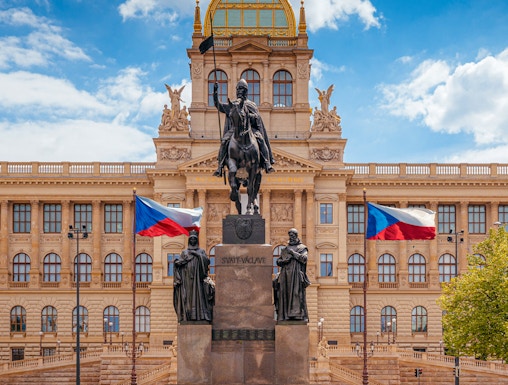 Equestrian statue in front of Prague National Museum with Czech flags.