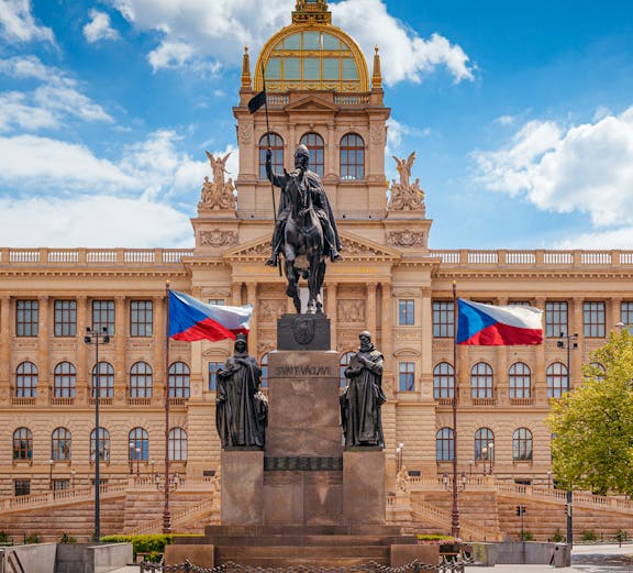 Equestrian statue in front of Prague National Museum with Czech flags.
