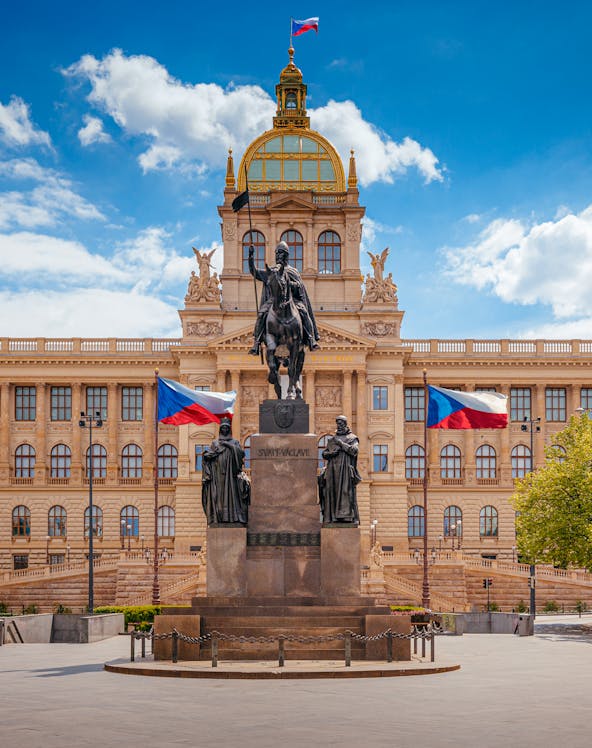 Equestrian statue in front of Prague National Museum with Czech flags.