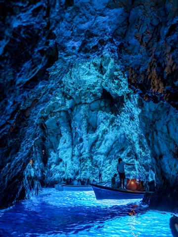 Boats with tourists exploring the illuminated Blue Cave in Croatia.