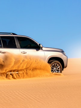 SUV driving through desert sand during dune bashing tour.