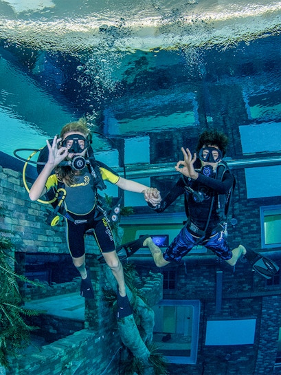 Divers exploring underwater cityscape at Deep Dive Dubai.