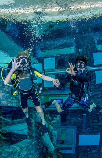 Divers exploring underwater cityscape at Deep Dive Dubai.