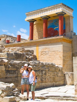 Visitors taking a selfie at Knossos Palace, Crete, with ancient ruins and frescoes in the background.