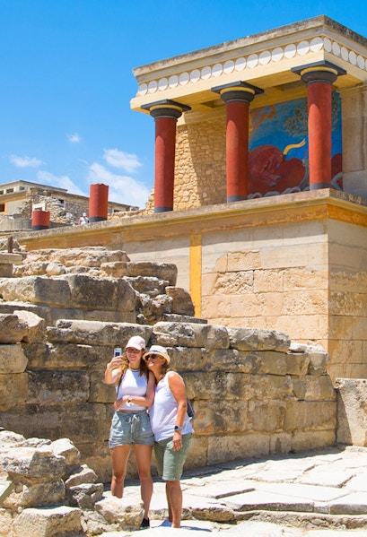 Visitors taking a selfie at Knossos Palace, Crete, with ancient ruins and frescoes in the background.