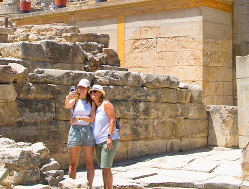 Visitors taking a selfie at Knossos Palace, Crete, with ancient ruins and frescoes in the background.