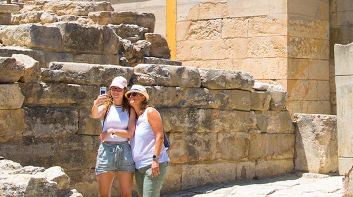 Visitors taking a selfie at Knossos Palace, Crete, with ancient ruins and frescoes in the background.