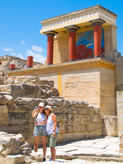 Visitors taking a selfie at Knossos Palace, Crete, with ancient ruins and frescoes in the background.
