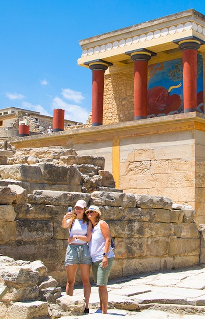 Visitors taking a selfie at Knossos Palace, Crete, with ancient ruins and frescoes in the background.