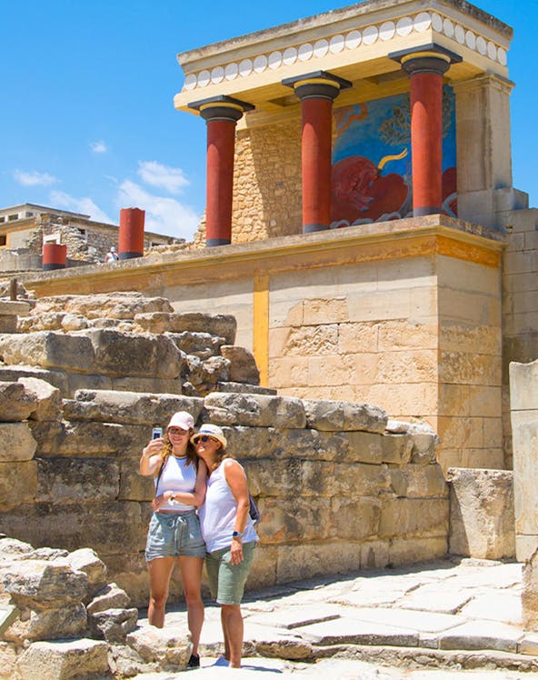 Visitors taking a selfie at Knossos Palace, Crete, with ancient ruins and frescoes in the background.