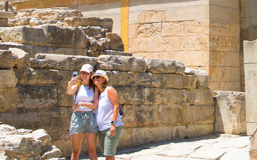 Visitors taking a selfie at Knossos Palace, Crete, with ancient ruins and frescoes in the background.