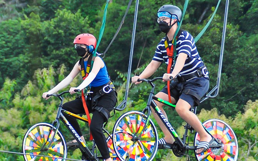 Two people riding bicycles on a high wire at Xtreme Park Langkawi.
