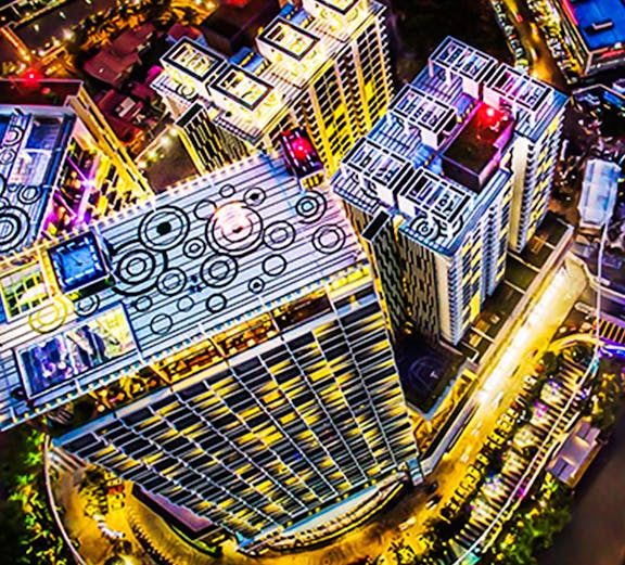 Aerial view of The Shore Sky Tower in Melaka, illuminated at night with surrounding cityscape.