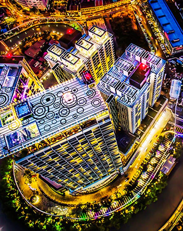 Aerial view of The Shore Sky Tower in Melaka, illuminated at night with surrounding cityscape.