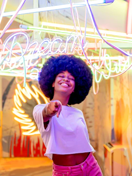 Smiling person pointing in front of colorful neon lights at Ikono exhibit.