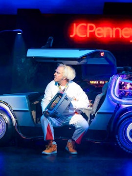 Man in white suit with futuristic car on stage, Olivier Award Winners.
