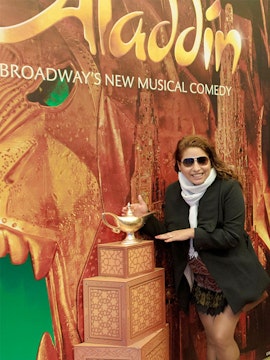 Person posing with Aladdin Broadway show poster and magic lamp display.