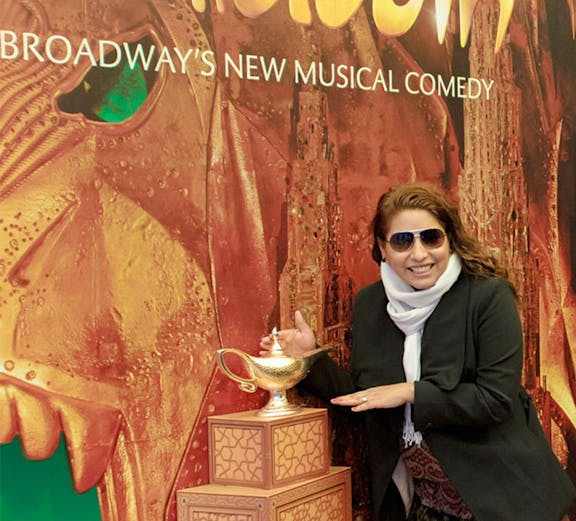 Person posing with Aladdin Broadway show poster and magic lamp display.