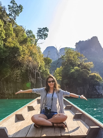 Person sitting on a boat in Kilim Geoforest Park Langkawi, surrounded by lush cliffs and water.