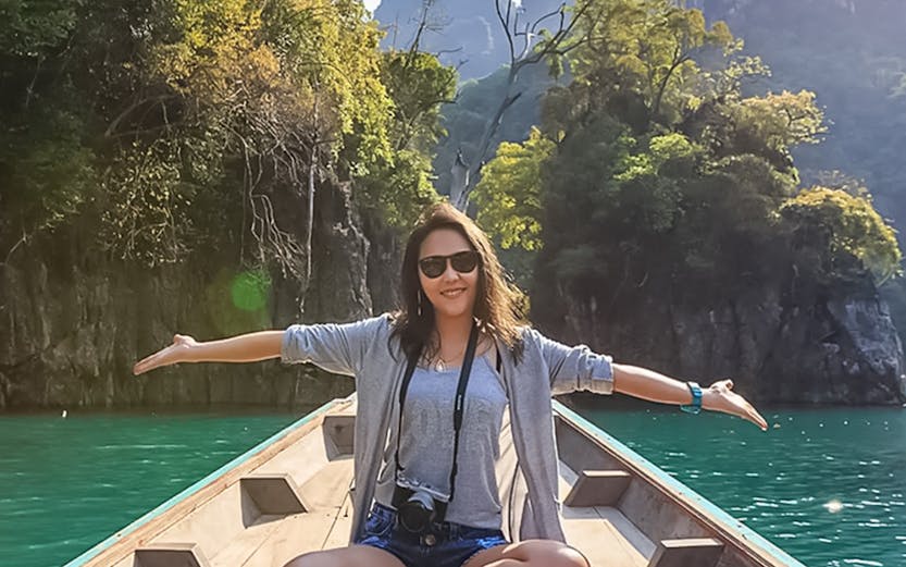 Person sitting on a boat in Kilim Geoforest Park Langkawi, surrounded by lush cliffs and water.