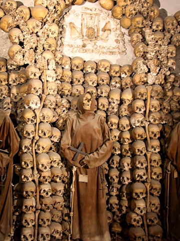 Capuchin Crypt in Rome with monk statue and skulls on display.