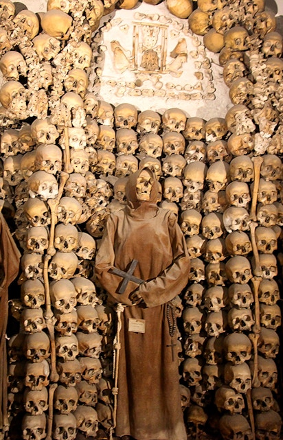 Capuchin Crypt in Rome with monk statue and skulls on display.