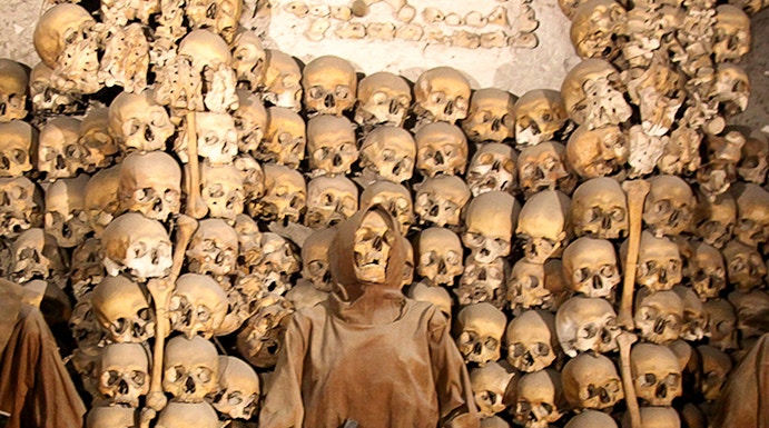 Capuchin Crypt in Rome with monk statue and skulls on display.