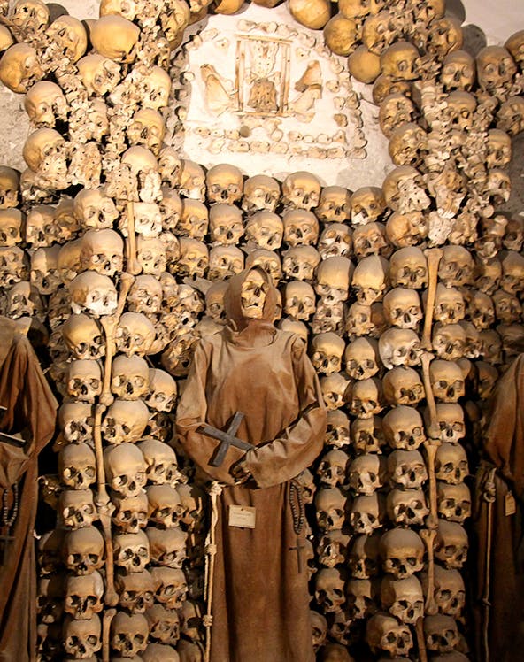Capuchin Crypt in Rome with monk statue and skulls on display.