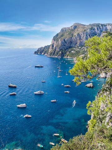 Boats sailing near rocky cliffs and clear blue waters of Capri, Italy.