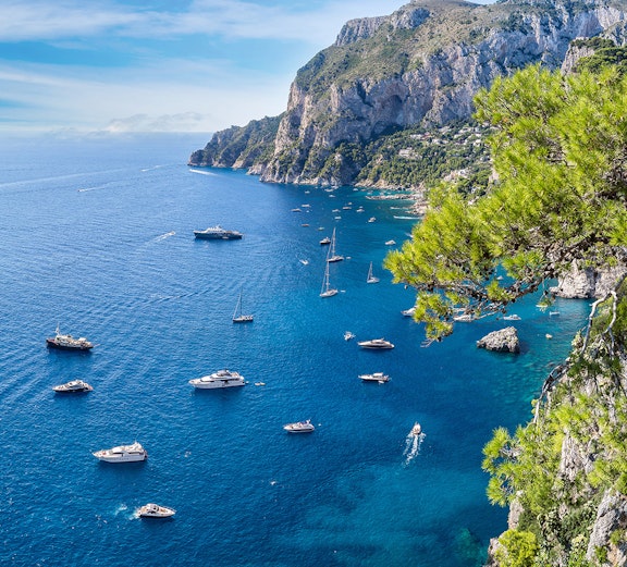Boats sailing near rocky cliffs and clear blue waters of Capri, Italy.