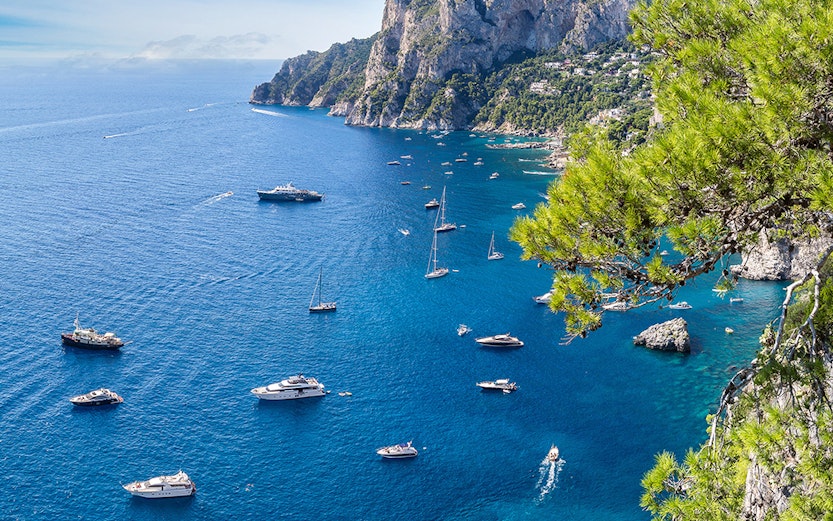 Boats sailing near rocky cliffs and clear blue waters of Capri, Italy.