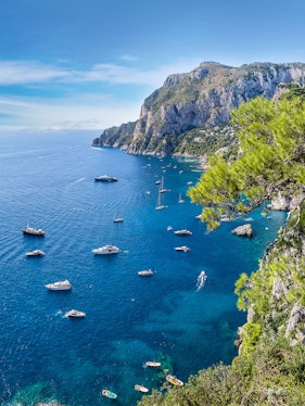 Boats sailing near rocky cliffs and clear blue waters of Capri, Italy.