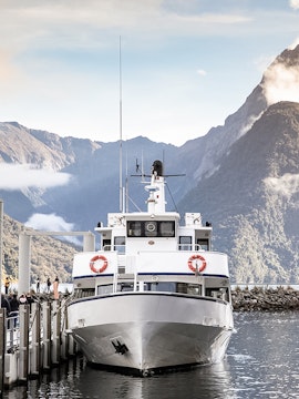 Cruise boat docked at Milford Sound with mountain backdrop.