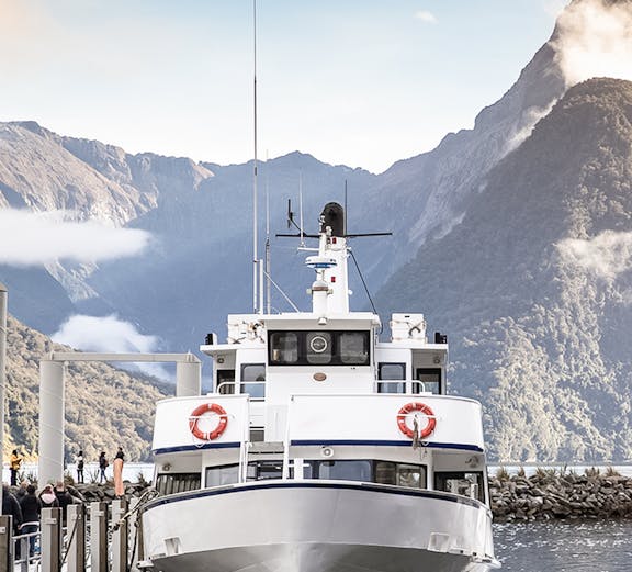 Cruise boat docked at Milford Sound with mountain backdrop.