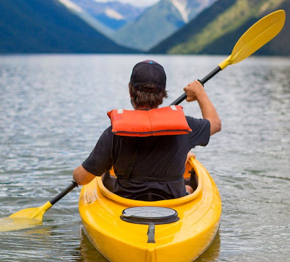 Person kayaking on a lake in Rotorua with mountains in the background.