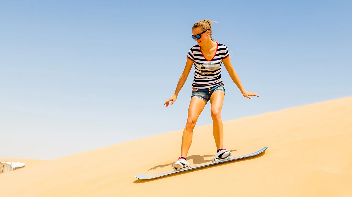 Person sandboarding down a dune in Dubai desert.