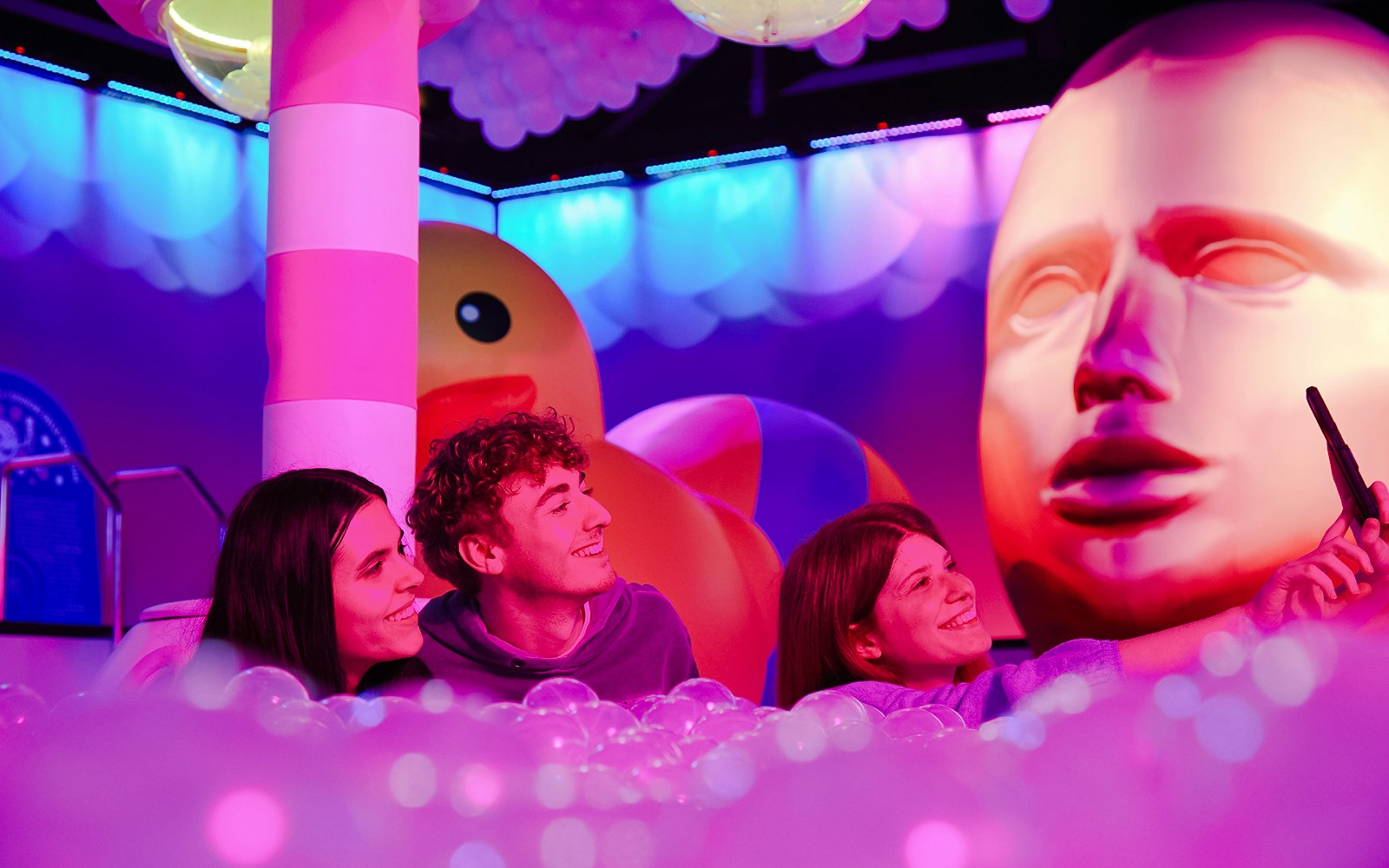 Visitors taking a selfie at Bubble Planet exhibit in Washington DC with colorful lights and giant sculptures.