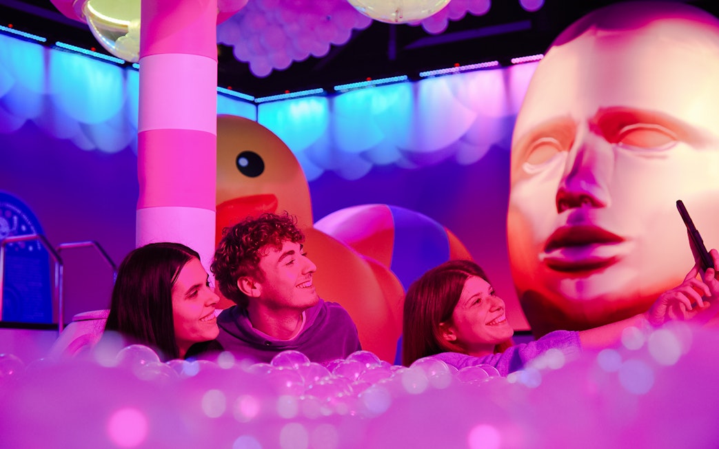 Visitors taking a selfie at Bubble Planet exhibit in Washington DC with colorful lights and giant sculptures.