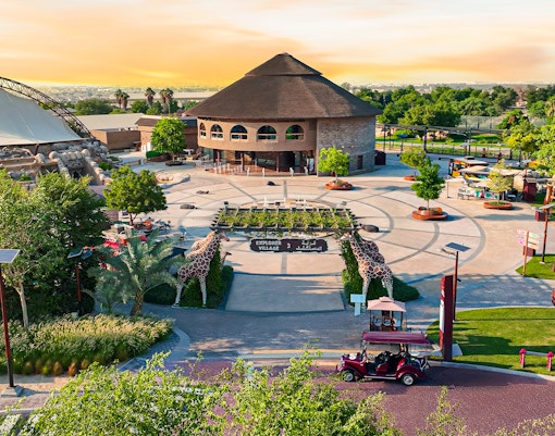 Explorer Village entrance at Dubai Safari Park with giraffe sculptures and lush greenery.