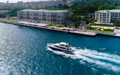 Bosphorus yacht cruising past Dolmabahçe Palace, Istanbul, aerial view.