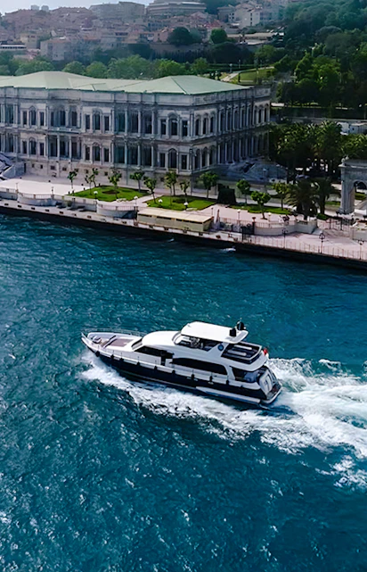 Bosphorus yacht cruising past Dolmabahçe Palace, Istanbul, aerial view.