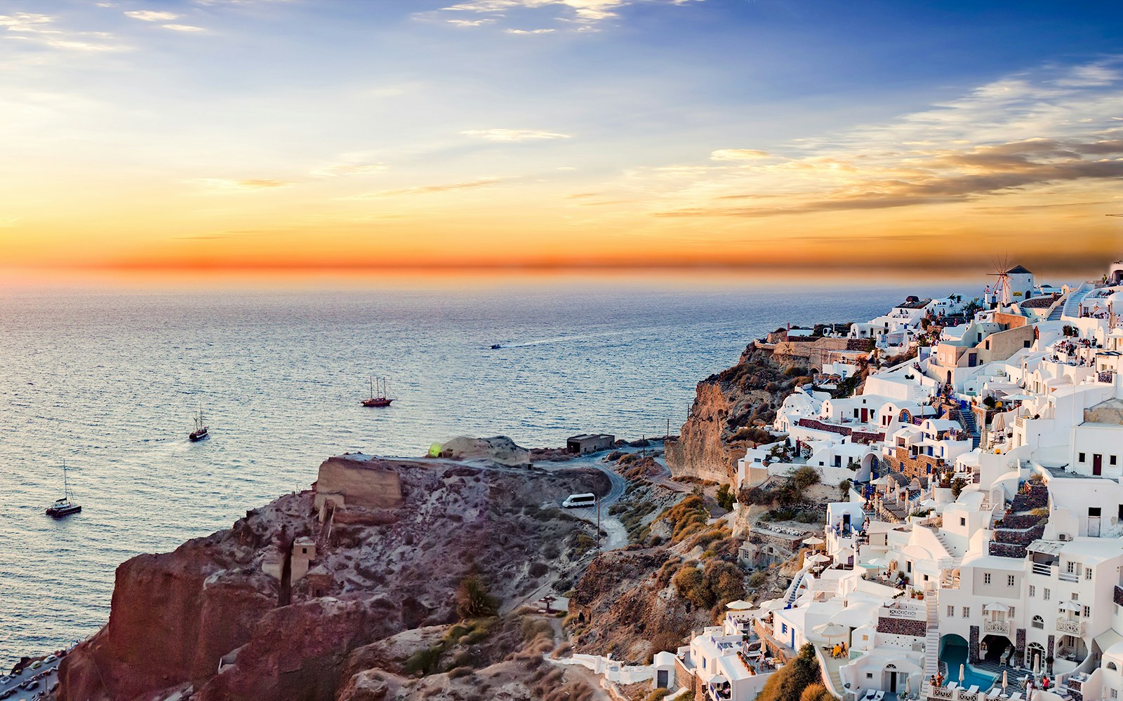 Panoramic view of Santorini's white buildings on cliffs at sunset, overlooking the Aegean Sea.