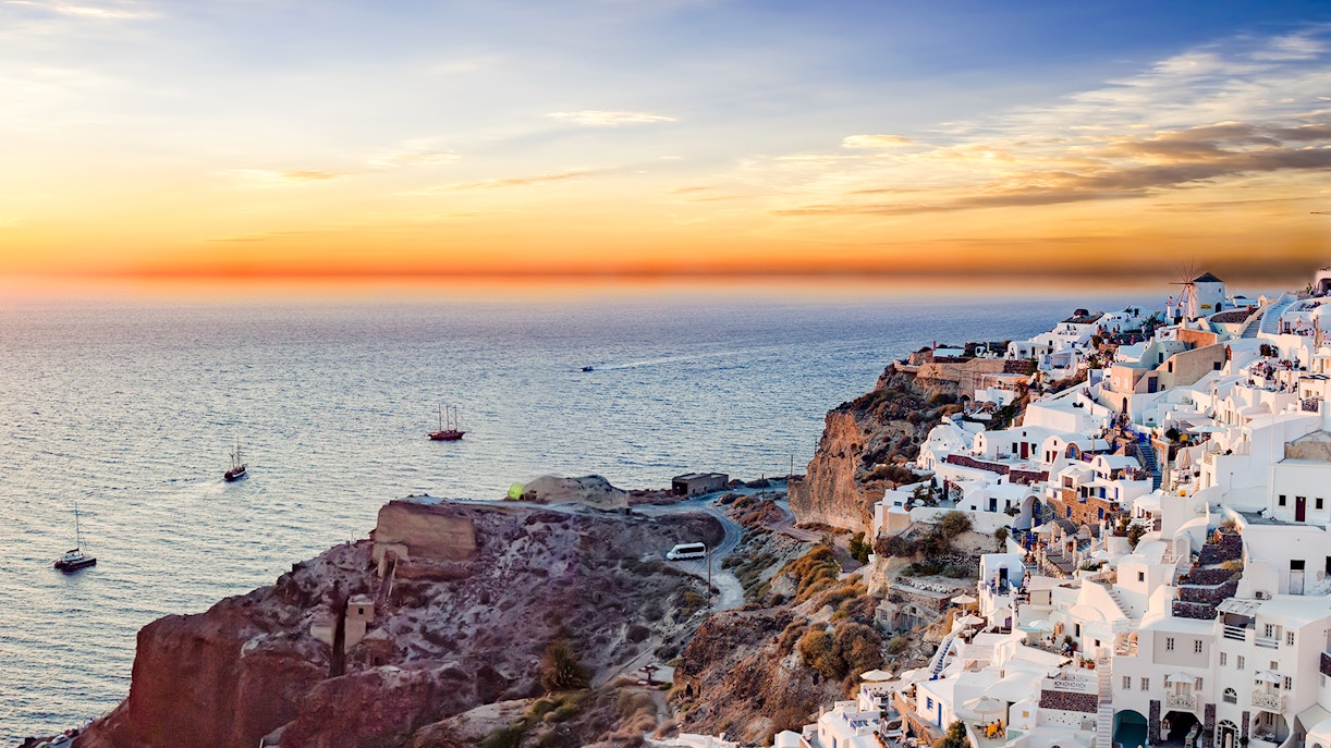 Panoramic view of Santorini's white buildings on cliffs at sunset, overlooking the Aegean Sea.