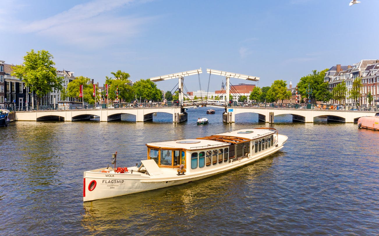 Saloon boat cruising through Amsterdam canal with historic buildings in view.