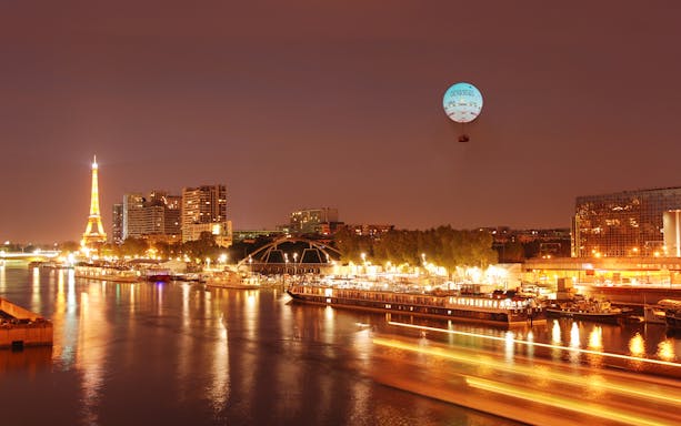 Ballon de Paris Generali floating over Seine River with Eiffel Tower in view.
